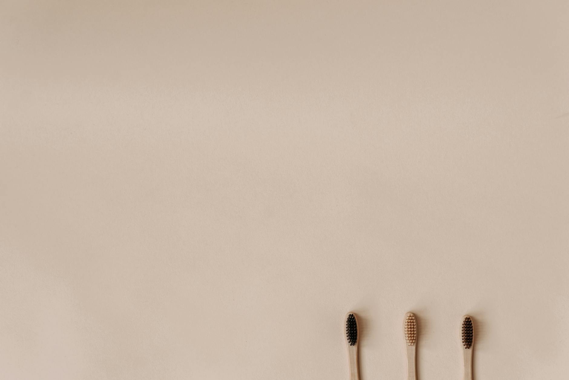 Three bamboo toothbrushes on a minimal beige background promoting eco-friendly oral care.