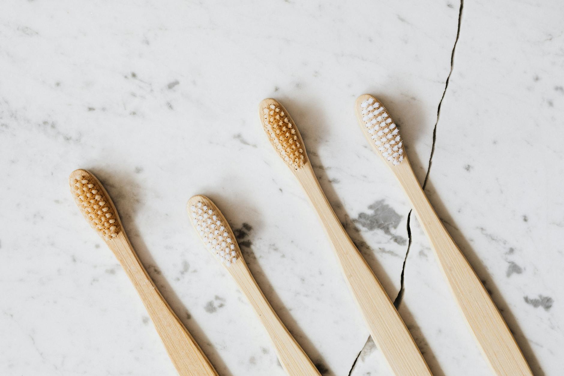 Flat lay of four bamboo toothbrushes on marble surface emphasizing eco-friendly dental hygiene.