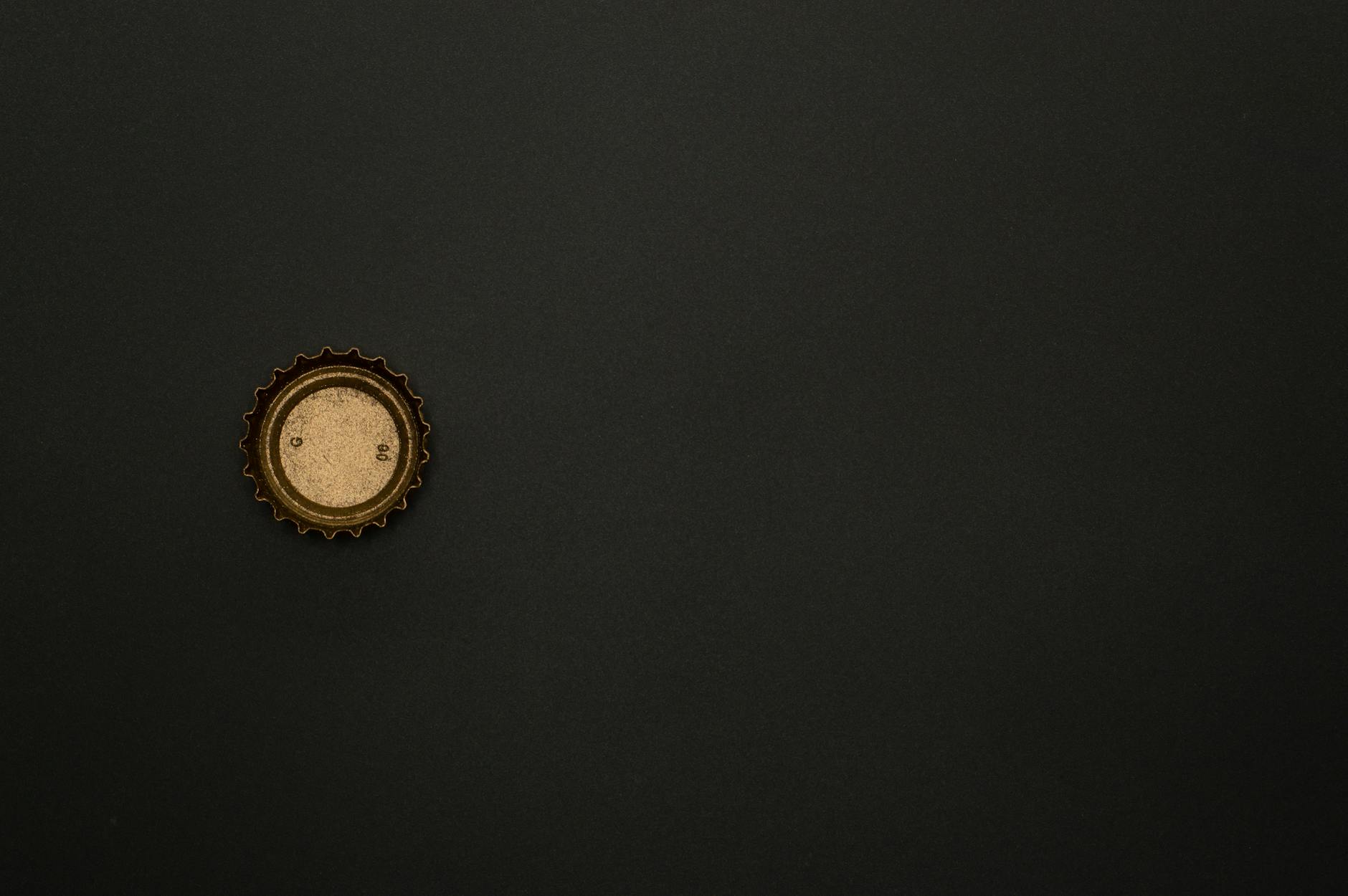 Minimalist image of a golden bottle cap on a dark surface, providing ample copy space.