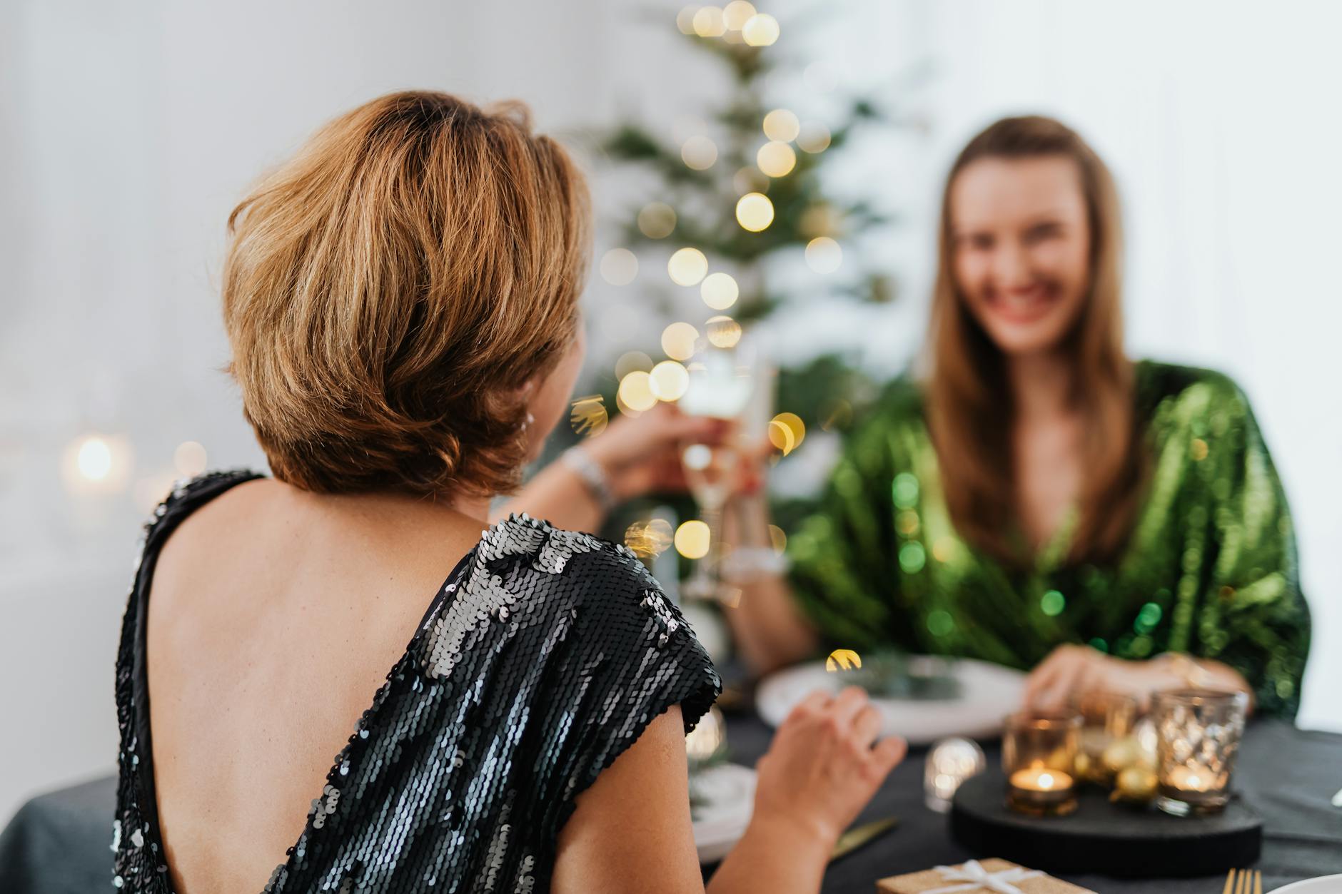 Two women celebrating indoors with a festive toast, dressed in glamorous attire.