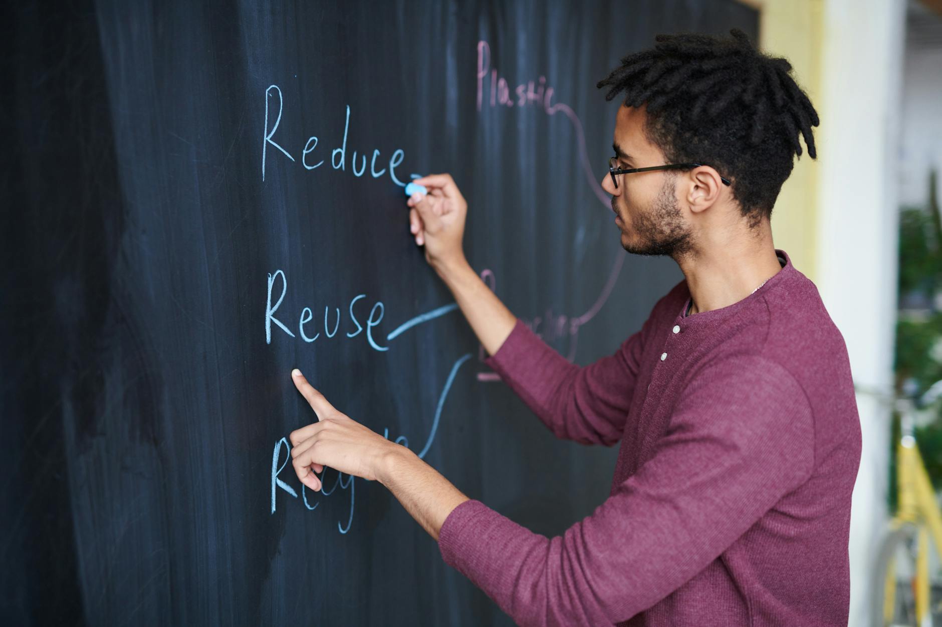Adult male writing environmental phrases on a chalkboard, focused on sustainability and recycling concepts.
