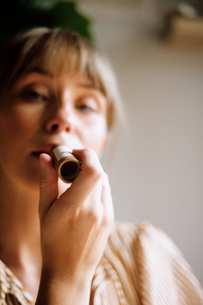 A woman using eco-friendly lip balm in natural lighting, promoting sustainable beauty.