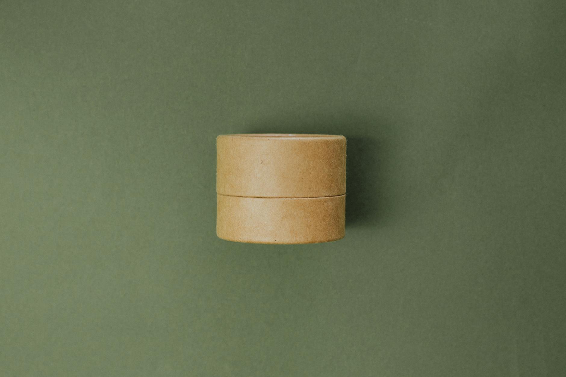 Eco-friendly cardboard cosmetic container on a minimalist green background. Sustainable beauty concept.
