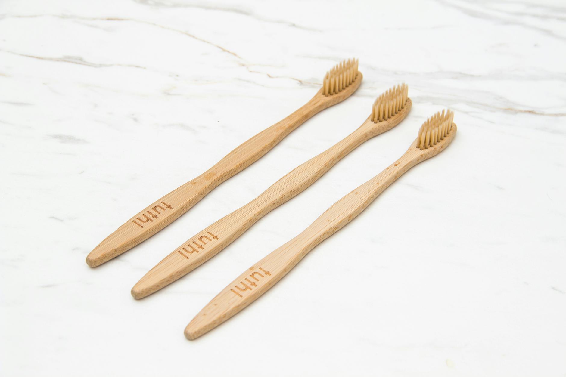 Three eco-friendly wooden toothbrushes arranged on a marble surface.