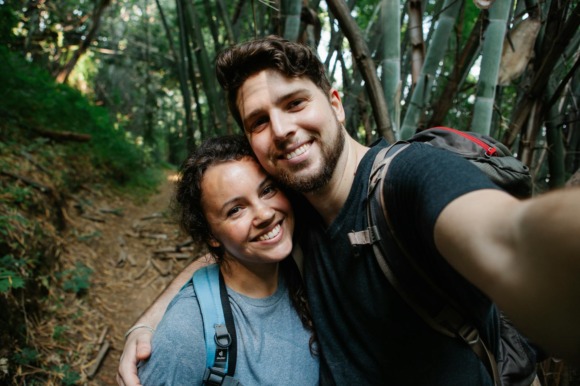 A joyful couple taking a selfie during a hike through a lush forest trail.