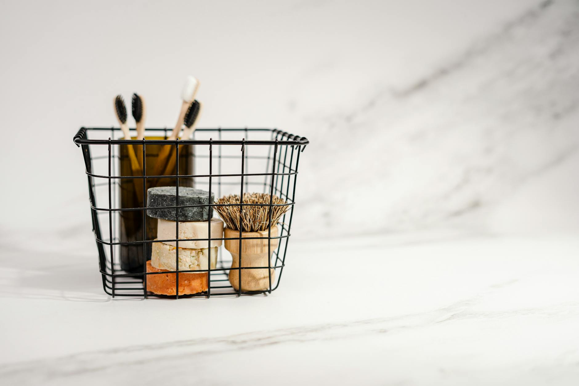 Minimalist setup of eco-friendly toiletries in a black wire basket on a marble surface.
