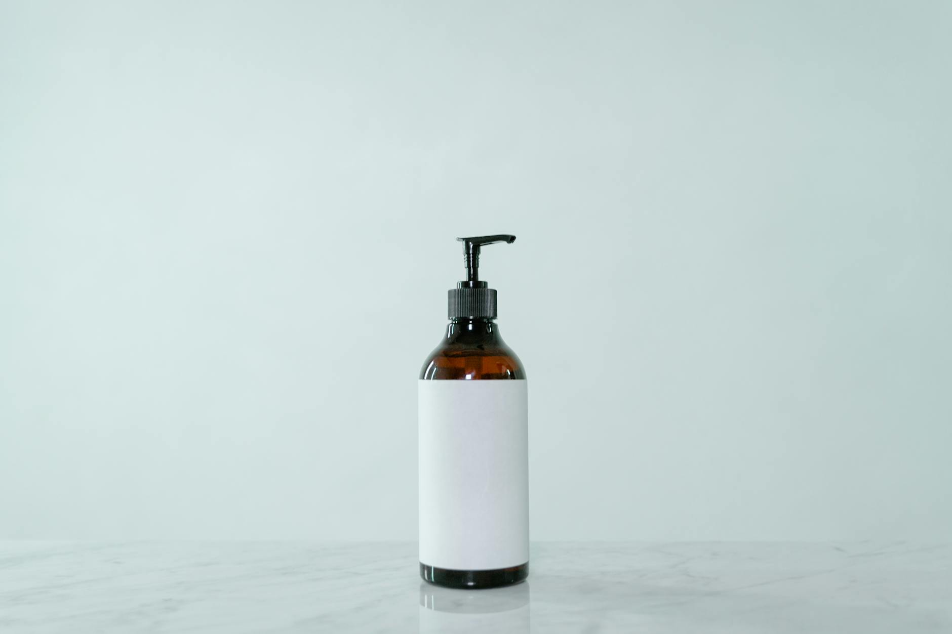 Minimalist display of a brown glass pump bottle with blank label on a light surface.